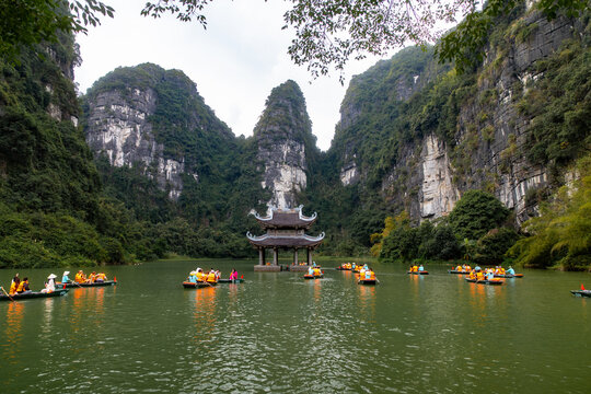 View of tranquil waters reflecting the ancient pagoda amidst towering limestone karsts, as rowboats glide gently in Trang An, Hoa Lu, Vietnam.
