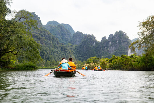 View of serene waters reflecting the majestic limestone karsts as rowboats glide, carrying passengers through the lush, verdant landscape, Trang An, Vietnam.