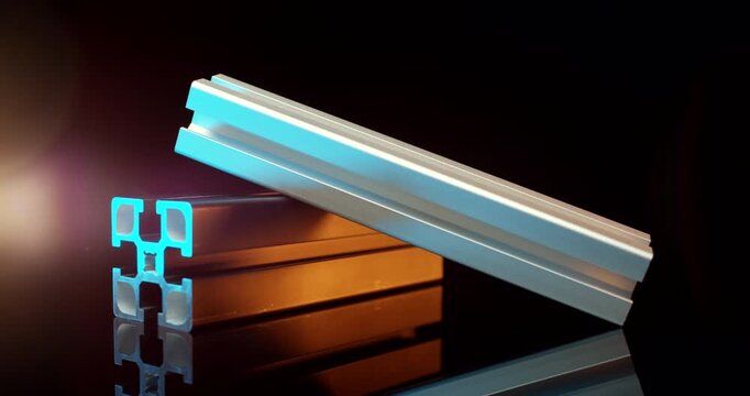 Two industrial aluminum t-slot extrusion profiles leaning together with blue and orange light on black background
