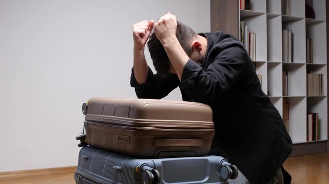 Man trying to close his overfilled suitcase, pressing down with his fists on top of the luggage while feeling frustrated and stressed about packing for a trip
