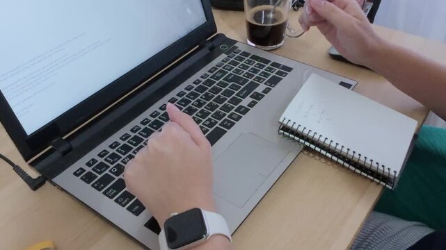 Student taking handwritten notes in a notebook during an online class or study session with a laptop