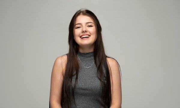 Young woman confidently smiling and laughing, expressing happiness and cheerful emotion while posing in a studio