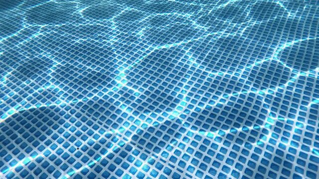 Close view of a blue swimming pool floor with clear water and sun reflections. Concept for summer, recreation, wellness, travel, sport, pool care, cleanliness, and background design.