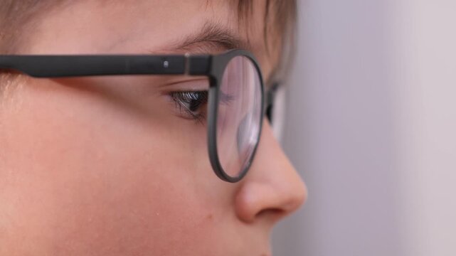 Young child in black prescription glasses, close up profile of eye and lens reflecting light, conveying childhood vision care, focused learning, screen use and eye health