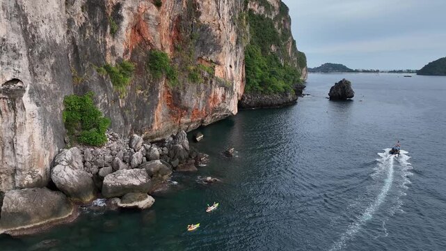 Aerial view of rugged cliffs meet the turquoise sea, boats cutting through the water, creating a dynamic scene of adventure and natural beauty, Halong Bay, Vietnam.