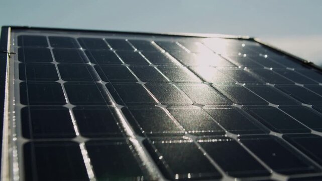 Solar panel surface reflecting sunlight, showcasing photovoltaic cells with clear sky and distant mountains in the background, emphasizing renewable energy technology and sustainability