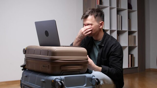 Man experiences burnout and fatigue while working remotely on a laptop, using stacked luggage as a temporary desk, symbolizing the stress of a digital nomad lifestyle and constant travel