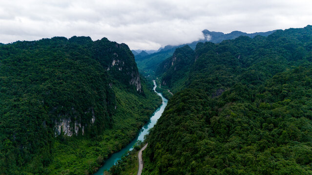 Aerial view of the winding river cutting through the lush, verdant valley beneath the brooding sky, Dark Cave, Qung Binh, Vietnam.