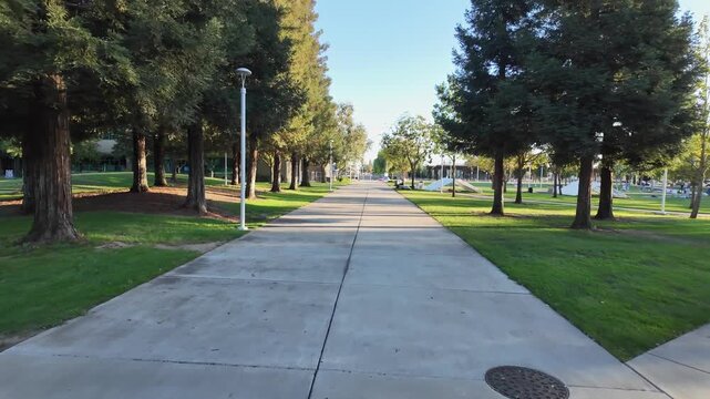 Smooth camera movement following a concrete pathway through the campus of Modesto Junior College in California, with tree-lined lawns and modern buildings visible under a clear blue sky
