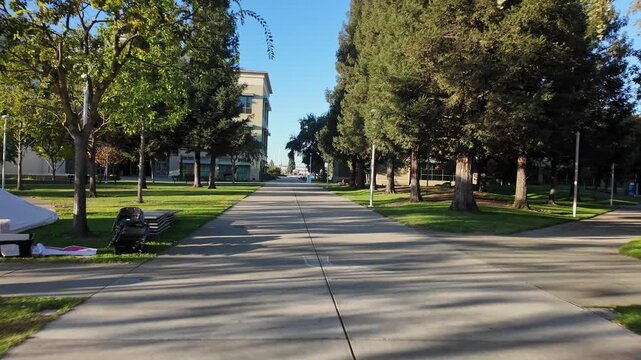 Forward-moving shot down a concrete path on the empty campus of Modesto Junior College in California, with long shadows from the trees on a sunny morning and no people present