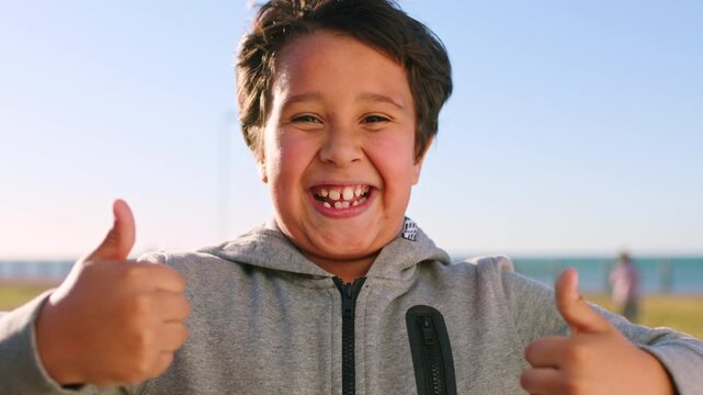 Face, kid and thumbs up in nature for success, agreement and feedback with celebration. Hand gesture, like and boy outdoor with thank you emoji, yes sign and excited child with portrait at park