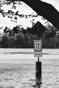 A monochrome photograph of a navigation sign standing in a calm lake scenery