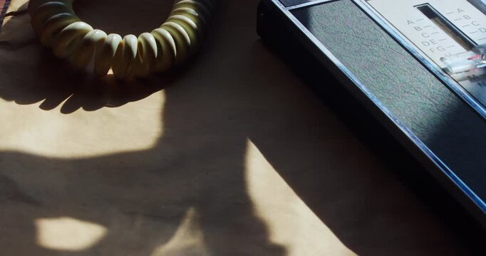 Close-up of a person using a pop-up contact book and a rotary phone, seen only through the shadow of the coiled cord. Moody, cinematic noir style.