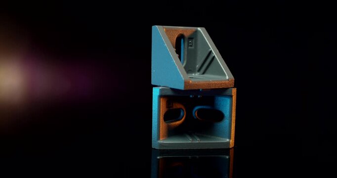 Two grey industrial metal corner bracket connectors stacked on reflective black surface with blue lighting