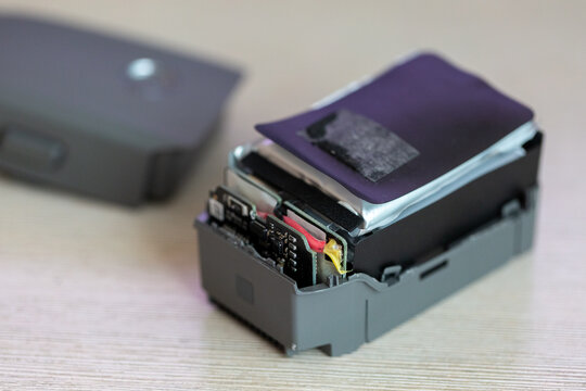 Macro shot of the internal components of an open grey drone battery on a table, highlighting the reflective foil battery cell and wiring