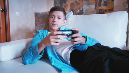 cinematic of teen boy sitting on the sofa and plays a game on a console, have fun and enjoy © vla