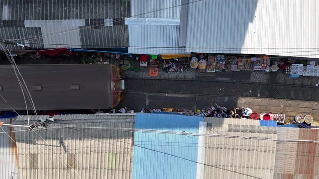 Aerial view of a train passing through the vibrant Maeklong Railway Market, a scene of commerce amidst the railway tracks, Maeklong, Thailand.