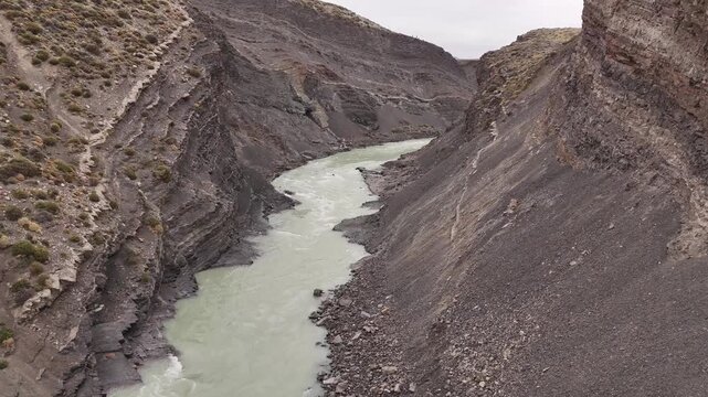 Aerial view of a river's milky waters carving through the steep, rocky canyon walls in a display of nature's relentless power, Chalten, Argentina.