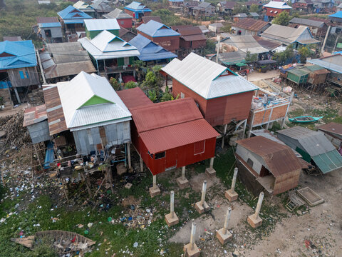Aerial view of houses on stilts reflected in the murky water, a testament to resilience against the elements, Tonle Sap, Cambodia.