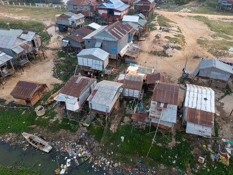 Aerial view of weathered stilt houses cluster along the water's edge, reflecting in the murky water, Tonle Sap, Cambodia.