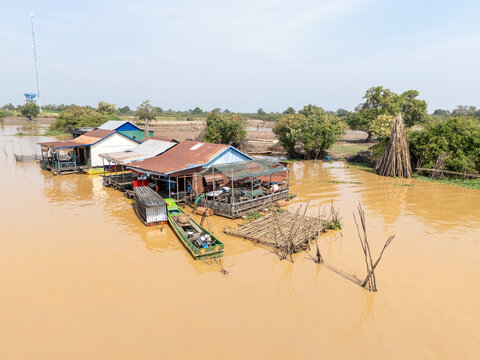 Aerial view of stilt houses cluster over the murky waters, where a green boat sits moored, reflecting the vibrant life of the floating village, Tonle Sap, Cambodia.