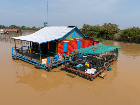 Aerial view of a vibrant floating house with red walls and blue trim contrasts against the muddy waters of Tonle Sap, Tonle Sap, Cambodia.