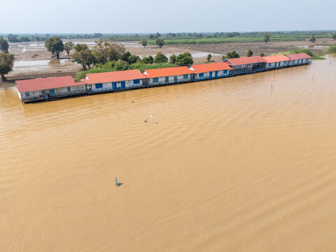 Aerial view of a long, low-lying structure with a vibrant red roof mirroring in the muddy waters of the lake, Tonle Sap, Cambodia.