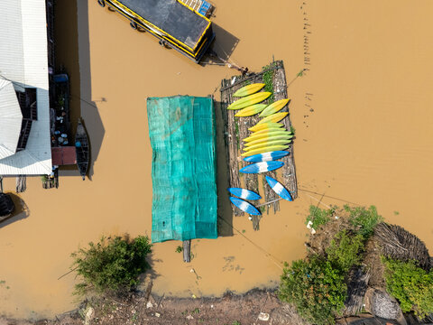 Aerial view of a floating village where colorful kayaks rest on a wooden platform amidst the muddy waters of the river, Tonle Sap, Cambodia.
