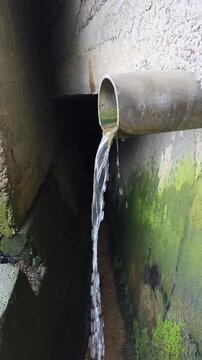 Water Rushes Through Underground Tunnel. Rapid Water Movement Reveals Hidden Drainage System. Drainage Worker Assesses Water Speed While Explorers Document Textured Walls And Algae Growth