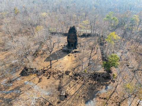 Aerial view of the ancient Prasat Neang Kmao temple rises amidst the dry, golden-brown forest, a stark contrast to the lush green patches, Prasat Neang kmao, Cambodia.