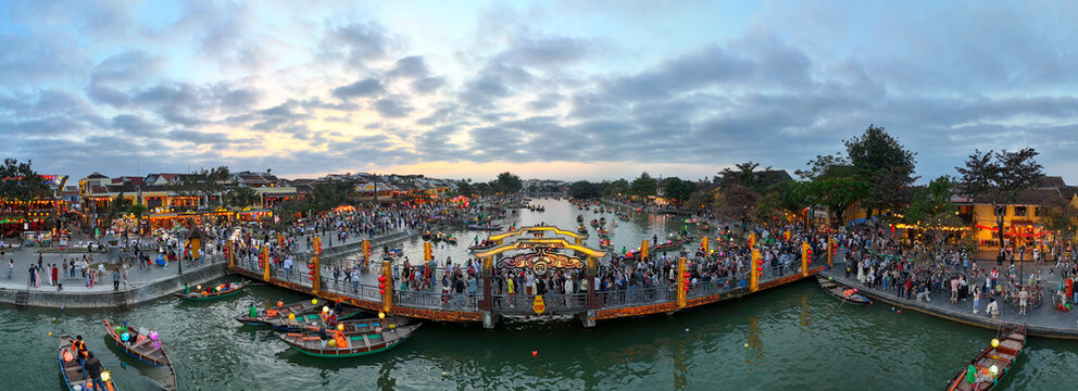 Aerial view of the bustling Japanese Covered Bridge illuminated against the fading evening light, crowded with people and boats, Hoi An, Vietnam.