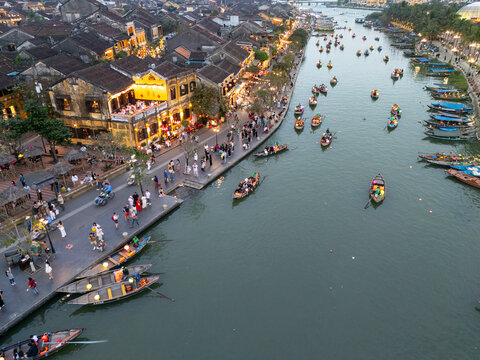 Aerial view of vibrant Hoi An Ancient Town, where traditional boats glide along the Thu Bon River, reflecting the warm glow of lantern-lit streets, Hoi An, Vietnam.