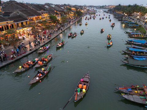 Aerial view of the tranquil Thu Bon River glimmers with floating lanterns and traditional boats, framed by the ancient architecture of Hoi An, Vietnam.