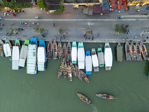 Aerial view of boats docked along the Thu Bon River, their white tops contrasting with the dark wood and the green water, Hoi An, Vietnam.
