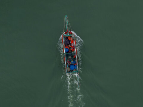 Aerial view of a solitary fishing boat slicing through the still, dark waters, leaving a foamy trail in its wake, Da Nang, Vietnam.
