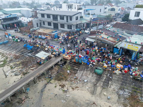Aerial view of a bustling market scene unfolds near the waters edge, vibrant chaos against the muted tones of the architecture, Da Nang, Vietnam.