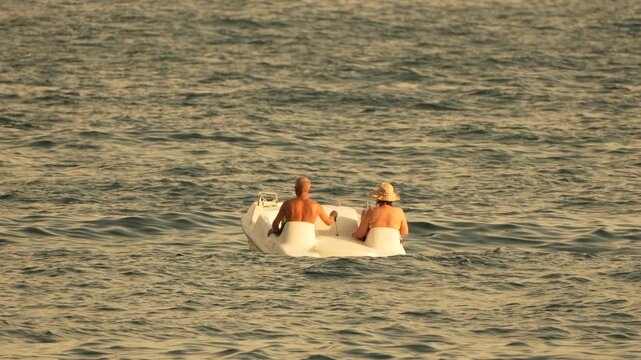 Elderly couple pedal boat ocean, enjoying leisure vacation in summer.