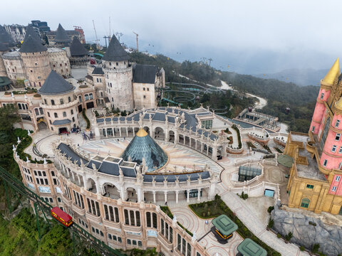 Aerial view of European-style architecture with the domed roof building and castle-like structures, contrasting with the misty mountains in the background, Ba Na Hills, Vietnam.