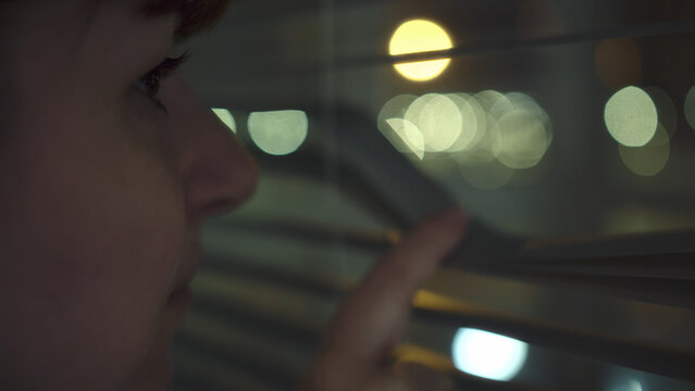 Woman Looking Through Window Blinds at Night with City Lights, have fun and enjoy