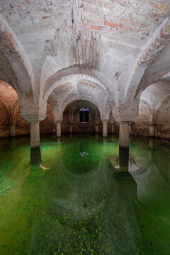 View of eerie green water reflecting the arched brick ceiling and stone columns of an ancient subterranean chamber, Ravenna, Italia.