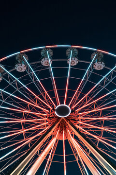 View of a Ferris wheel ablaze with bright red and blue lights against the dark sky creating a vibrant, dynamic spectacle, Cesenatico, Italia.