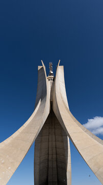 View of the concrete monument soaring upwards against the clear, bright sky, a symbol of remembrance and reflection in Tipasa, Algeria.
