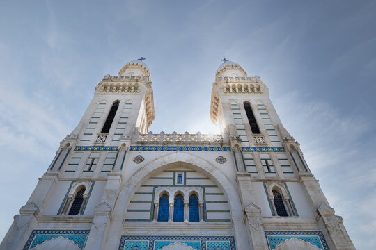 View of the Basilique Saint Augustin's twin towers reach towards the blue sky, adorned with intricate white stone and turquoise accents, standing tall, Annaba, Algeria.