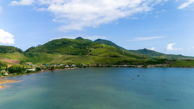 Aerial view of lush green mountains meet the tranquil waters of the lagoon, a serene landscape punctuated by a quaint oyster farm, tt. Lang Co, Hue, Vietnam.