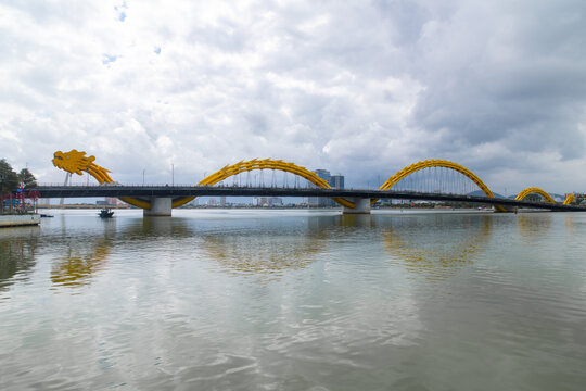 View of the majestic Dragon Bridge spans the tranquil river, its golden scales shimmering under the vast sky, reflecting in the still waters, Da Nang, Vietnam.
