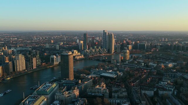 Golden hour aerial establishing shot of the Thames River flowing through Westminster, with Millbank Tower skyscraper and residential buildings