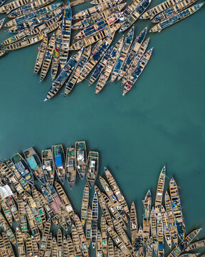 Aerial view of numerous boats clustered tightly on the water, a vibrant tapestry of wood against the turquoise sea, Sekondi Takoradi, Ghana.