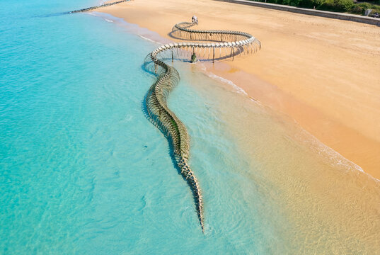 Aerial view of Serpent d'ocean sculpture contrasting the turquoise water and sandy beach, Saint-Brevin-les-Pins, France.