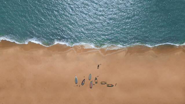 Aerial view of boats resting on the sandy beach meeting the turquoise ocean with foamy waves, Lobito, Angola.