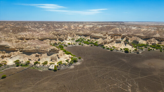 Aerial view of rugged cliffs casting long shadows over the arid landscape, with sparse vegetation clinging to life amidst the rocks, Namibe, Angola.